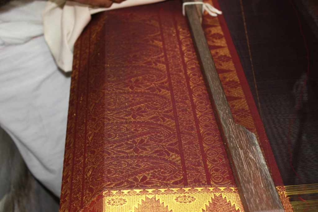 Red and gold patterned silk being woven on a loom in Kanchipuram